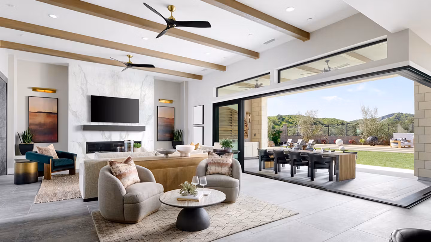A modern and spacious living room with a cozy seating area, a dining table, and large windows overlooking a lush outdoor landscape.